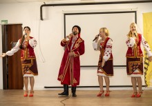 Дівчата у національному вбранні та хлопець у козацькому костюмі співають на сцені.