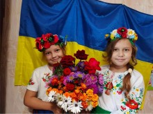 Дві дівчинки тримають букет живих квітів на фоні прапора України