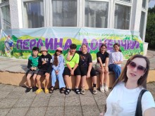 Діти сидять біля фасаду будівлі, на якому висить банер з надписом "Перлина Донеччини", жінка робить селфі.