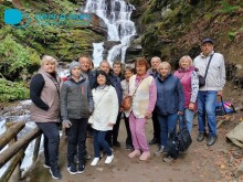 Спільне фото переселенців з різних громад. Позаду водоспад. Чоловіки та жінки одягнені у теплий одяг.