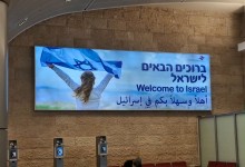 Інформаційне табло в аеропорту з написом «Welcome to Israel» трьома мовами та зображенням дівчинки, яка тримає прапор Ізраїлю