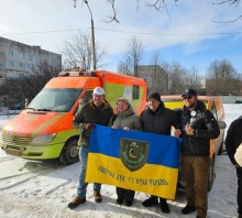 Міжнародні партнери та представники Донеччини тримають прапор Северської громади, позаду стоять отримані спеціалізовані автомобілі.