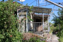 Пошкоджений будинок від обстрілів, але на подвір'ї цвітуть квіти.
