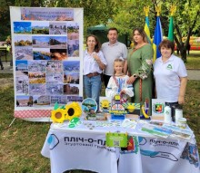 Стенд с фотографіями Торецької громади, стіл з сувенірною продукцією. Поруч стоять представники громад та діти.