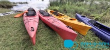 На березі річки стоїть чотири байдарки жовтого та червоного кольорів.