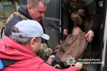 Люди разом з поліцейськм заносять лежачого чоловіка до евакомобіля