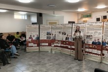 Представниця центру культури у вишиванці виступає з мікрофоном біля стенда «Смак дому: Авдіївська громада».