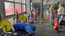 Спортсмени займаються у тренажерному залі. Один спортсмен займається зі штангою.