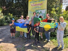 Діти тримають прапори України, Донеччини та Авдіївської громади на фоні банеру "Лімниця"