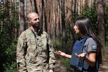 Журналістка спілкується з чоловіком у військовій формі. Чоловік посміхається, жінка жестикулює руками.