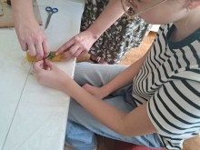 Учасниця майстер-класу прикрашає свічку з вощини, педагог допомагає закріпити стрічку та декоративні елементи