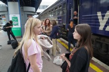 Дівчата розмовляють на пероні вокзалу. Позаду них потяг.