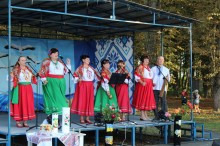Концерт. З програмою народної творчості виступають солісти. Жінки стоять на сцені у національному вбранні.