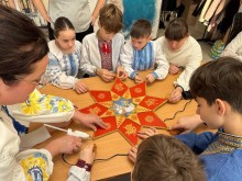 Діти у вишиванках разом із дорослим виготовляють велику восьмикутну різдвяну зірку з червоної тканини, оздоблену золотистими візерунками.