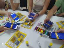 Учасники заходу сканують QR-код для онлайн-вікторини до Дня Конституції України. На столі — тематичні лепбуки та канцелярія.