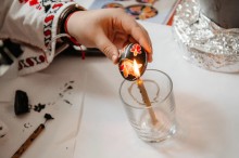 Розписана писанка, яку тримають біля свічки.