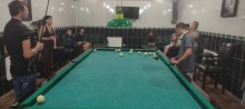 Молодь грає в більярд під час відпочинку на навчально-розважальному заході, інші учасники спостерігають, сидячи на диванах у залі.