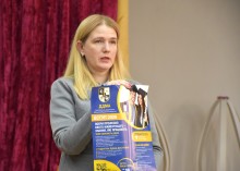 Презентація можливостей Донбаської державної машинобудівної академії та закладів професійно-технічної освіти Донеччини. Учасниця зустрічі стоїть на сцені та тримає буклет у руках.