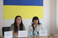 Під час відкритої зустрічі у Дружківській міській територіальній громаді: заступниця начальника Дружківської міської військової адміністрації Олександра Пахомова та начальниця управління соціального захисту населення Дружківської міської ради Ірина Бардар відповідають на запитання ветеранів та родин загиблих Захисників і Захисниць України. На задньому плані — Державний Прапор України.