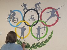 Студентка коледжу розписує стіну спортивної школи з олімпійською символікою в межах волонтерського мистецького проєкту.