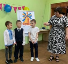 Першокласники Бахмутської громади під час урочистостей до Дня знань на освітній локації. Вчителька передає дзвіночок трьом майбутнім учням.