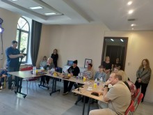 Матері Героїв та гості заходу сидять за столами в залі, чоловік з відеокамерою знімає захід