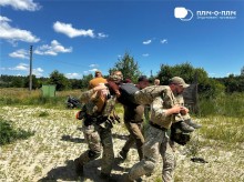 Інструктори тактичної медицини показують, як нести пораненого. Поранена людини знаходиться на плечах двох інструкторів, третій йде поруч та тримає за руку.