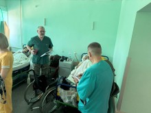 Лікарняна палата шпиталю. Двоє чоловіків у лікарняному вбранні стоять біля ліжка хворого, в руках тримають книжки
