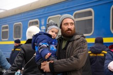 Чоловік тримає дитину на руках, стоячи на пероні біля евакуаційного потяга