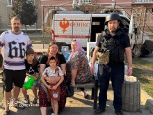 Родина з дітьми сидить на лавці, поруч - рятувальник групи "Фенікс"