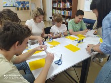 Діти й дорослі виготовляють лепбуки до Дня Конституції України: працюють із ножицями, клеєм і жовто-блакитними матеріалами.