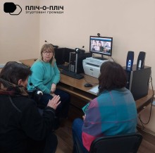 Учасники зустрічі в бібліотеці сидять перед ноутбуком, фахівці надають роз'яснення  онлайн