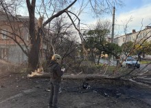 Правоохоронець стоїть біля пошкодженої будівлі та пошкодженого дерева