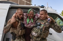Жінка похилого віку яку несуть поліцейські до броньованого автомобіля.