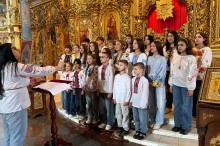 Диригентка керує дитячим хором у вишиванках під час виступу біля позолоченого іконостаса в храмі.