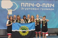 Група дівчат-спортсменок з Білозерської громади тримає прапор громади та позує на фоні банеру проєкту "Пліч-о-пліч"