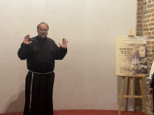 Священнослужитель у традиційному вбранні виступає з промовою поруч із головним плакатом виставки «Пам'ять, що звучить крізь віки».