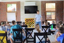 Тренер з шахматів розповідає дітям правила гри. Поруч стоїть дошка з шахматами.