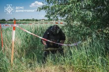 Мужній працівник ДСНС обережно несе снаряд на спеціальне місце. Чоловік міцної статури у засобах захисту.