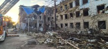 Зруйнована ворожим обстрілом багатоповерхова адміністративна будівля та пожежна машина поруч ліквідовує наслідки обстрілу.