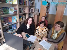 Учасники круглого столу «Тиждень читання: ідеї, що працюють» сидять в бібліотеці перед ноутбуком