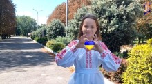 Дівчина у вишиванці робить серце руками, в якому знаходиться прапор України