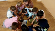 Група дітей зосереджено виконує завдання на підлозі, разом шукаючи правильні відповіді у веселій пізнавальній грі.