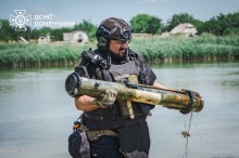 Фахівець розмінування у повній екіпіровці, виносить з водойми артилерійський снаряд.