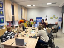 Учасники гри, сидять за столом на краю стола стоїть ноутбук,на столі солодощі,чай та гра.