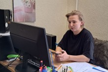 Дівчина у чорній футболці сидить за робочим столом перед монітором