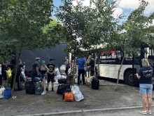 Евакуйовані люди стоять біля автобуса, який їх привіз. Багато валіз. Поруч з дорослими стоять діти.