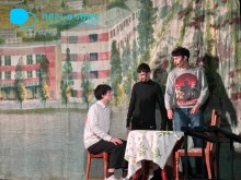 Троє акторів знаходяться на сцені. Один з акторів сидить на стільці за столом двоє стоять поруч.