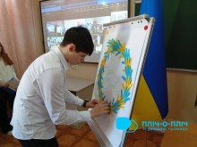 Хлопець у білій сорочці викладає вінок з жовто-блакитних стрічок