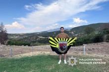 Хлопець стоїть на склоні гори та тримає прапор Головного Управління національної поліції з надписом Донеччина.